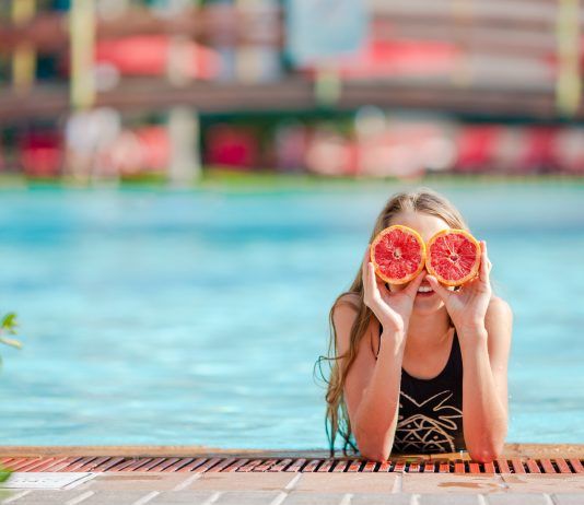 Las vitaminas que preparan nuestro cuerpo para el verano chica en la pisicna tapándose los ojos con un pomelo partido
