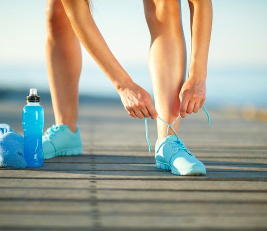 Estrategias nutricionales contra las agujetas: olvídate del agua con azúcar Chica atándose los cordones con botella de isotónica al lado